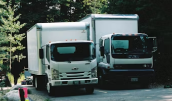White semi-truck driving fast on a highway with mountains and dark cloudy sky in the background.
